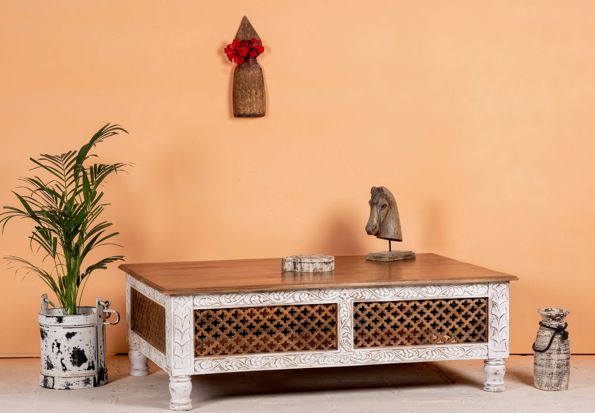 Decorative coffee table with intricate carvings in a room with a plant and wall art.