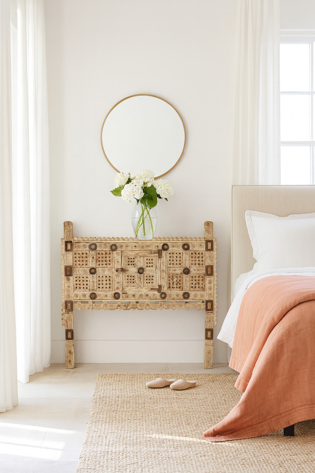 Bedroom with a wicker headboard, white bedding, and a round mirror.