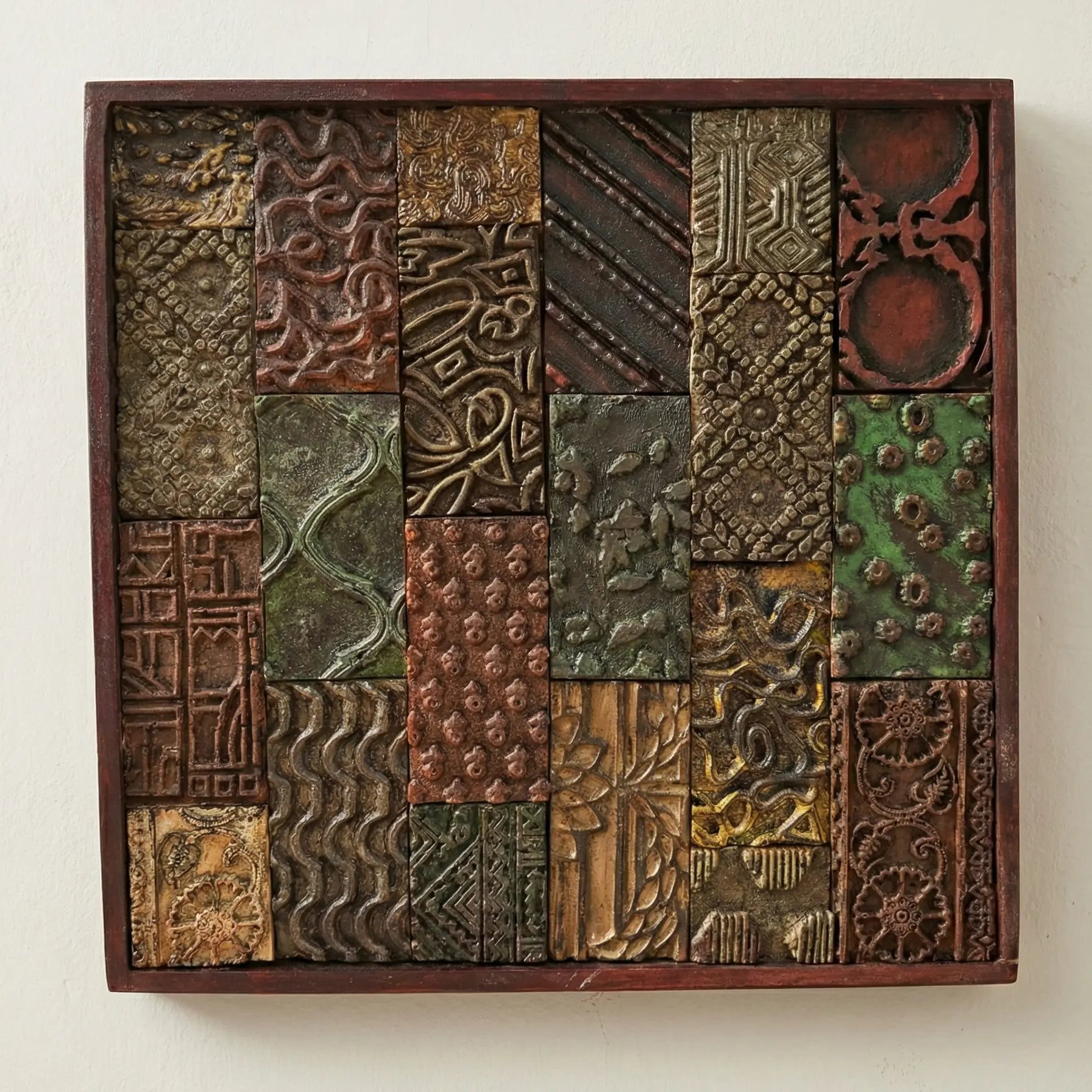 A square, framed wall art piece featuring a patchwork of textured tiles in earth tones like rust, green, bronze, and gold.A close-up view of a rustic mosaic artwork set inside a dark wooden frame. The piece consists of various rectangular relief tiles arranged in a grid. The tiles feature distinct raised patterns, including swirls, geometric lines, floral motifs, and abstract shapes, glazed in metallic and earthen shades of copper, moss green, and dark brown.vintage wall art wall decor home decor antique 