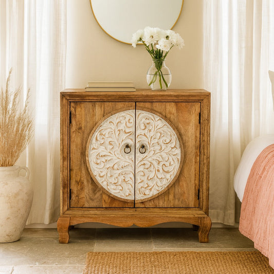 Wooden cabinet with decorative round door in a room setting with a vase of flowers and a mirror.
