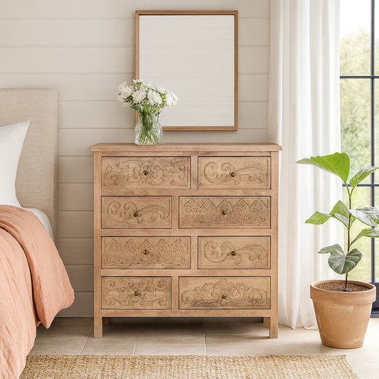 Wooden dresser with decorative carvings in a bedroom setting with a mirror and plant.