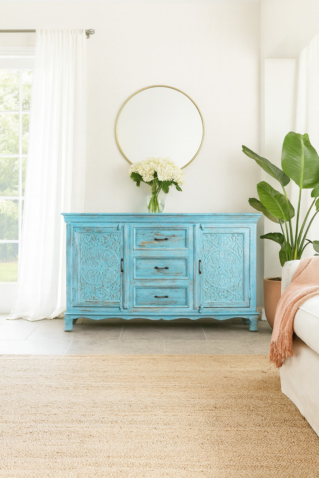 Blue distressed sideboard in a living room with a gold mirror and plants.