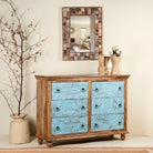 Wooden dresser with blue drawers next to a mirror on a wall.