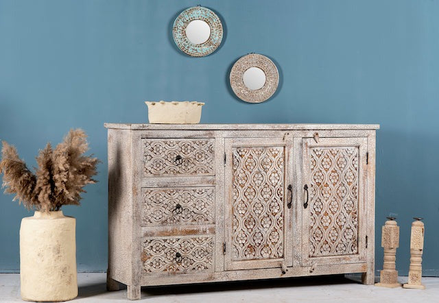 Wooden sideboard with decorative patterns against a blue wall with two round mirrors.